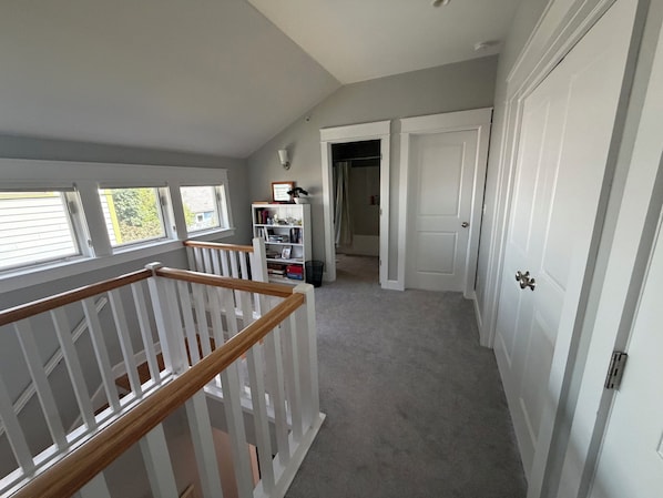 A hallway with a staircase, a bookshelf, and a door leading to another room.