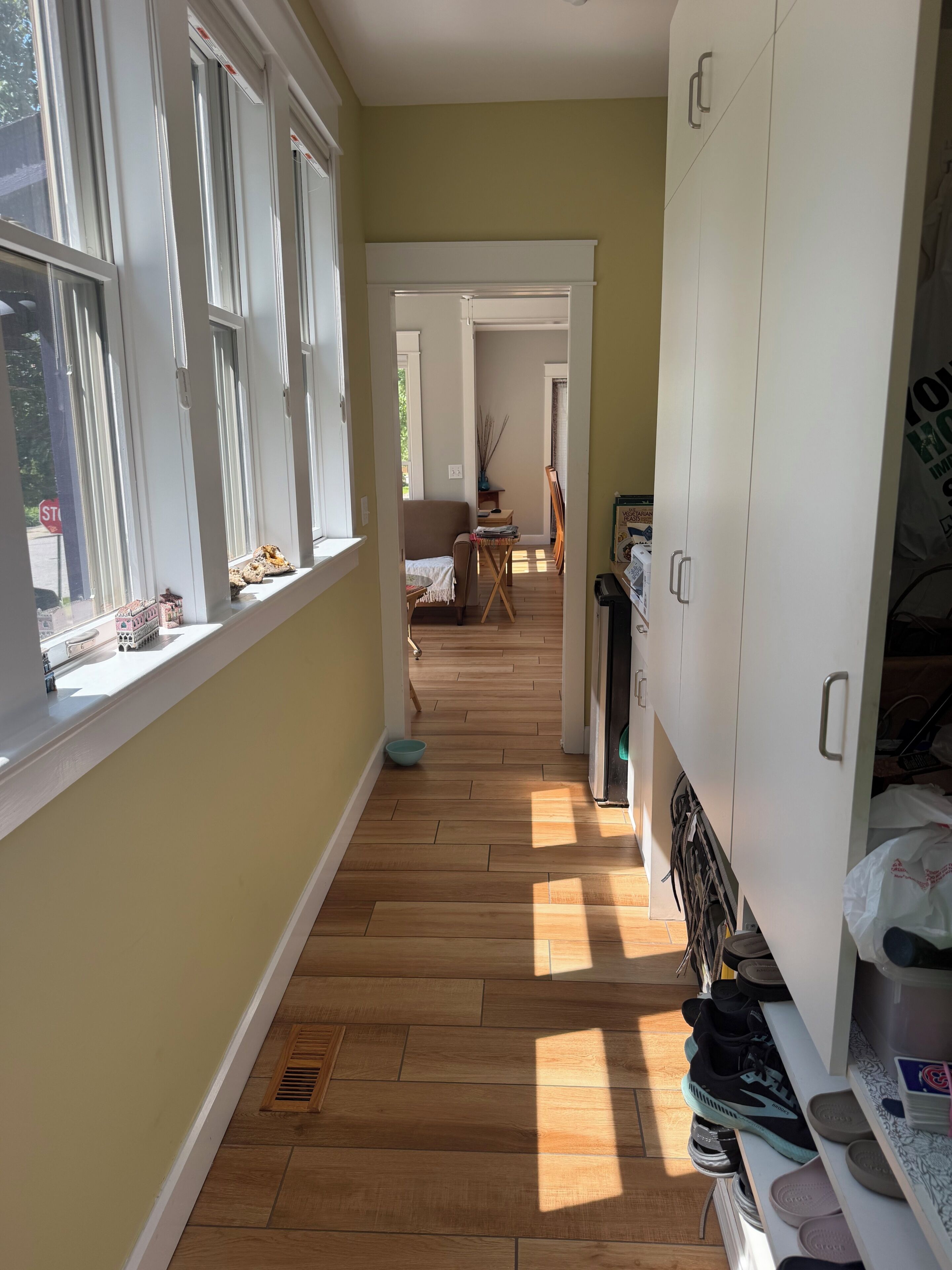 Un couloir avec un plancher en bois, une armoire blanche et une fenêtre donnant sur l’extérieur.