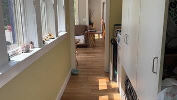 Un couloir avec un plancher en bois, une armoire blanche et une fenêtre donnant sur l’extérieur.