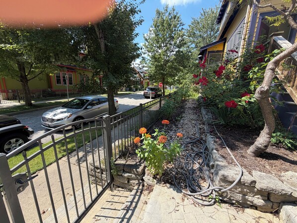 A residential street with a gated driveway, a garden with orange flowers, and a parked car.