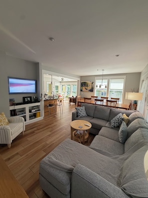 A modern living room with a grey sofa, a television, and a dining area with wooden furniture.
