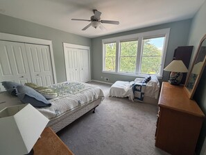 A bedroom with a bed, a dresser, a nightstand, a window with a view, and a ceiling fan.