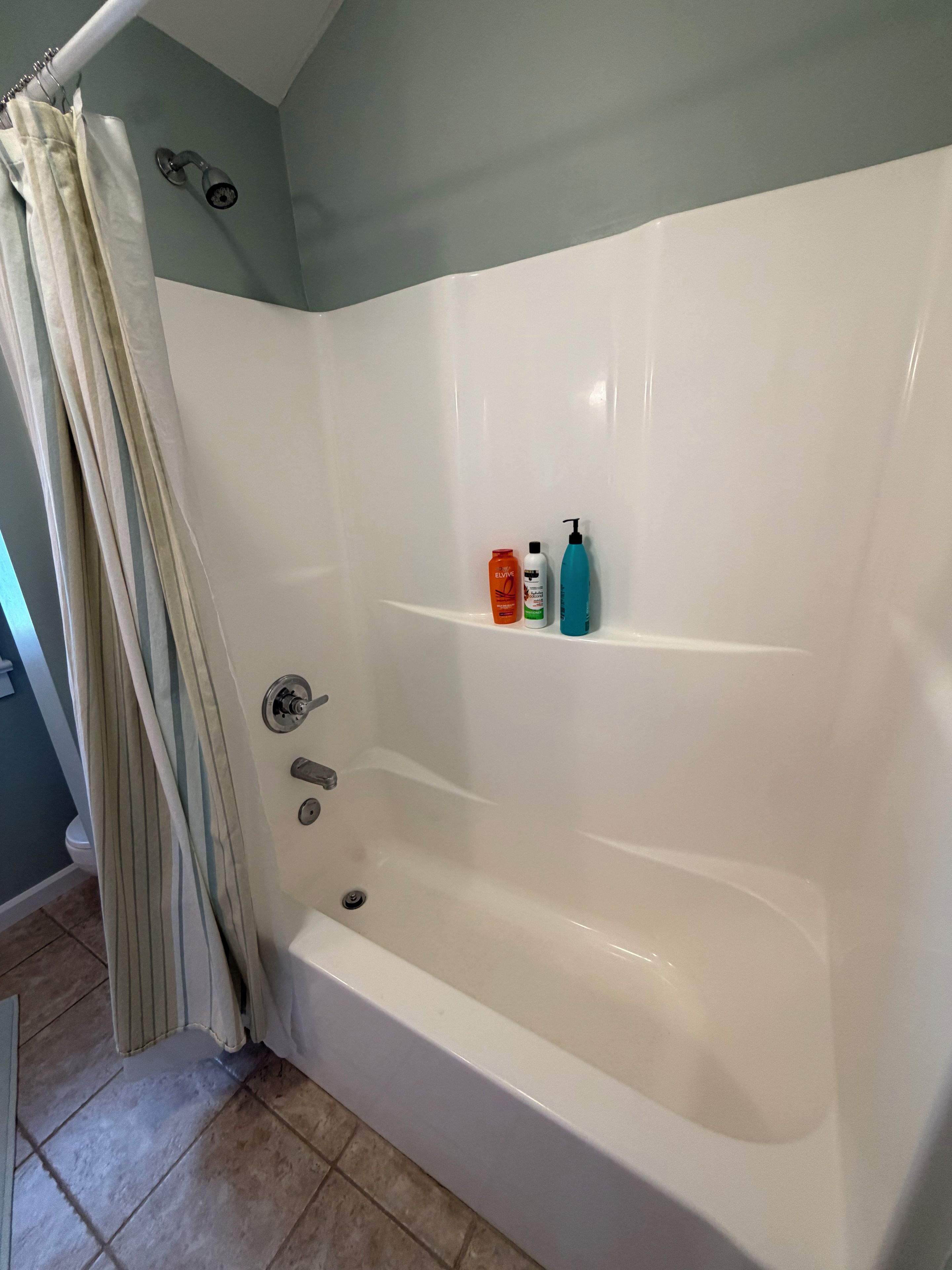A bathroom with a bathtub, a shower curtain, and toiletries on a shelf.
