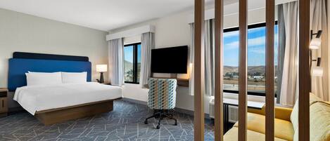 Habitación de hotel con una cama grande, un escritorio, un televisor y vistas al exterior.
