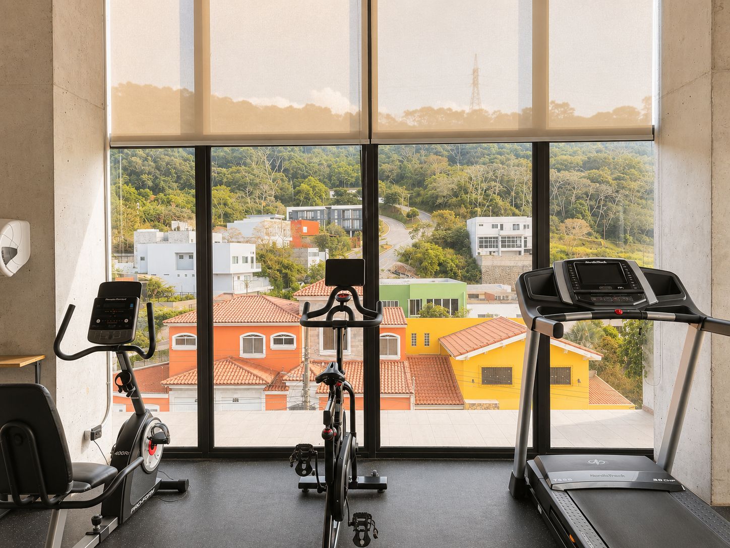 Ein Fitnessraum mit Ergometer und Laufbändern, große Fenster mit Blick auf Gebäude und Bäume.
