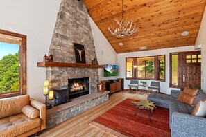 A living room with a stone fireplace, leather sofas, a red rug, and a wooden ceiling.