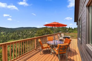A wooden deck with a table and chairs, an umbrella, and a view of a forested landscape. - Eagles Peak. Lake Arrowhead Modern Lake View Lodge. Pool Table AC Panorama Views (Lake Arrowhead)