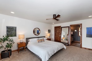 A bedroom with a bed, bedside lamps, a ceiling fan, a mirror, and a potted plant.