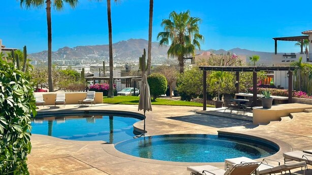 A swimming pool with lounge chairs, palm trees, and a view of distant mountains. - Villa Atardecer (Cabo San Lucas)