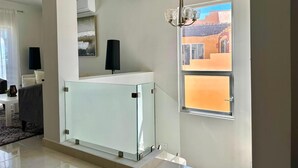 Una sala de estar moderna con un separador de vidrio, un ventilador de techo, una araña y un amplio ventanal con vista a un edificio.