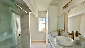A modern bathroom with a glass shower enclosure, two sinks with gold fixtures, and a large mirror. - Villa Atardecer (Cabo San Lucas)