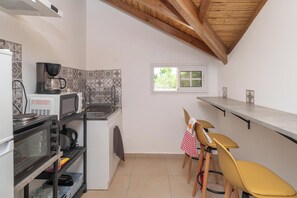 Eine kleine Küche mit Mikrowelle, Wasserkocher und Kaffeemaschine. Zwei Stühle und ein Fenster sorgen für natürliches Licht.