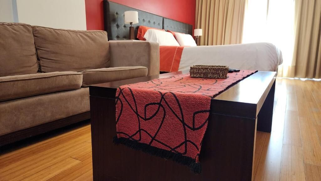A hotel room with a bed, a sofa, a nightstand, and a wooden floor.