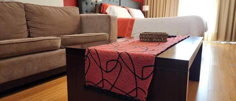 A hotel room with a bed, a sofa, a nightstand, and a wooden floor.