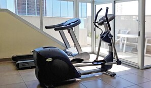 A home gym with an elliptical and a treadmill, a sliding glass door leading to a balcony with outdoor furniture. - Aparts Temporarios (Buenos Aires)
