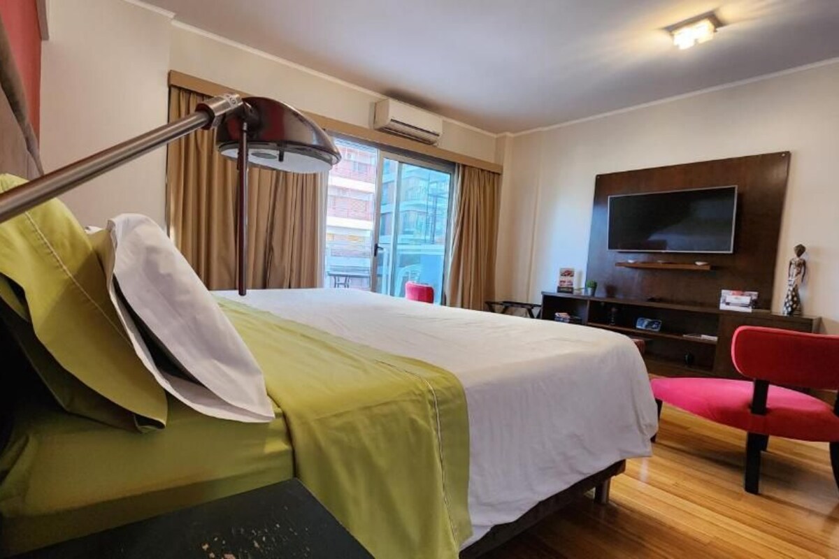 A hotel room with a bed, a desk, a chair, a TV, and a window.