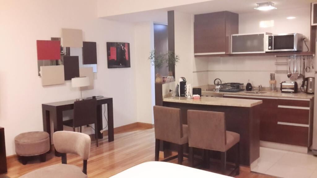 A modern kitchen with a microwave, toaster, and coffee maker. There is a dining area with a table and chairs.