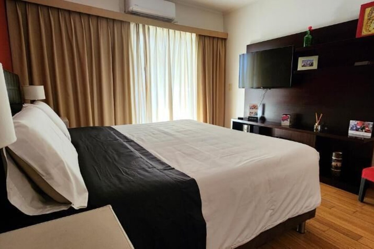 A hotel room with a bed, a television, a red chair, and a window with curtains.