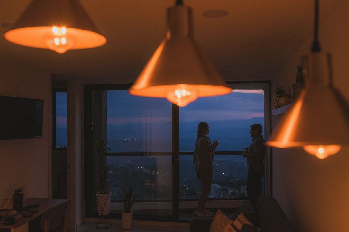A room with a large window, a dining table, and hanging pendant lights.