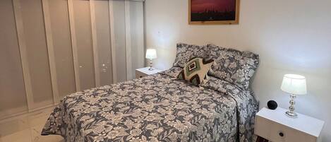 Un dormitorio con una cama, dos mesitas de noche, una lámpara de noche, un cuadro en la pared y una luz en el techo.