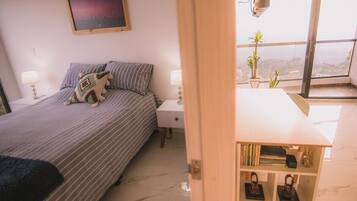 Un dormitorio con cama, mesitas de noche, estantería y ventana con vistas.
