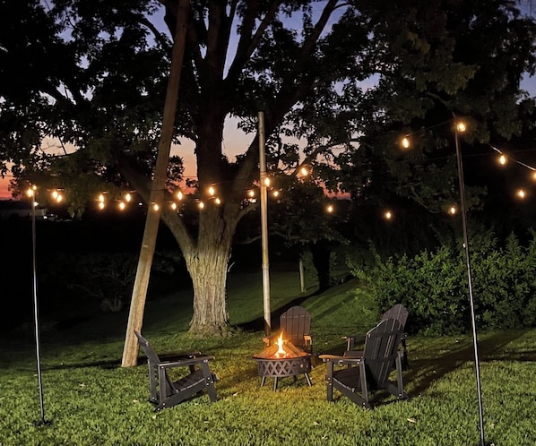 Un área de estar al aire libre con sillas y una chimenea, iluminada por guirnaldas de luces.