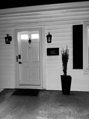 A white wooden house with a front door, two wall-mounted lanterns, a mailbox, and a potted plant. - Highland Hideaway - Tons of character, modern updates and art ! (Flemingsburg)