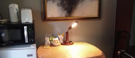 A small dining area with a table covered by a checkered tablecloth, a microwave, a toaster, and a painting on the wall.