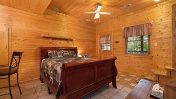 A wooden cabin bedroom with a bed, a chair, a ceiling fan, and a window with blinds.