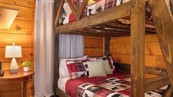 Una cama litera con colcha roja y negra, una mesita de noche con lámpara y una ventana con cortinas.