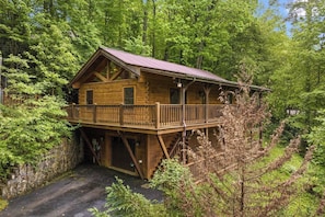 Una cabana de fusta amb un balcó, envoltada per un bosc dens.