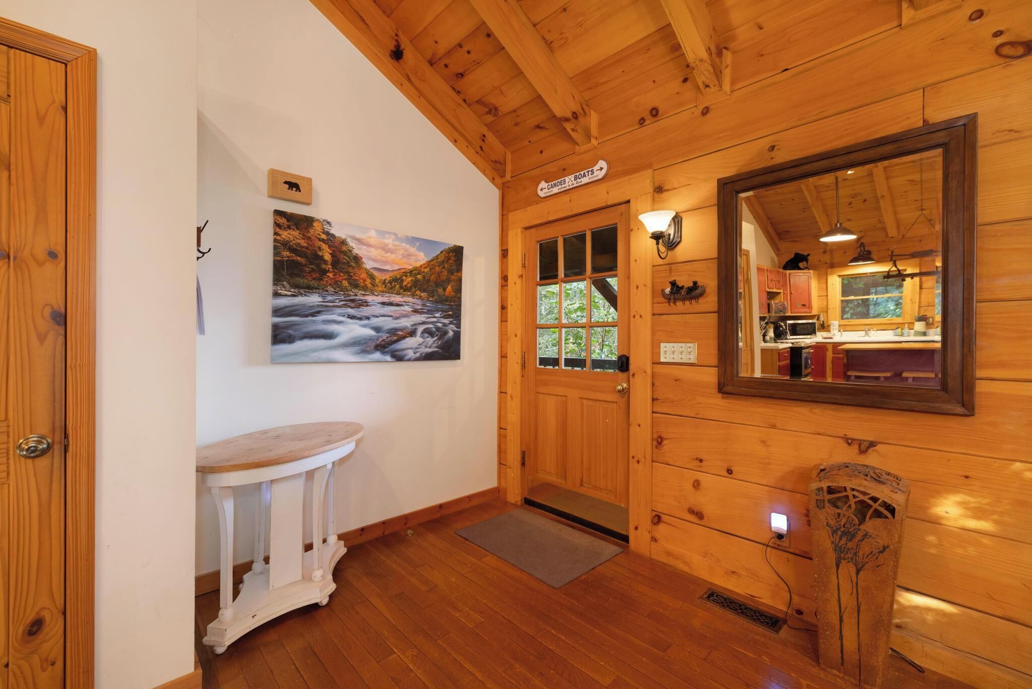 Interior em madeira com uma porta identificada como 'Canoas x Barcos', uma pintura de um rio e um espelho refletindo uma área de cozinha.
