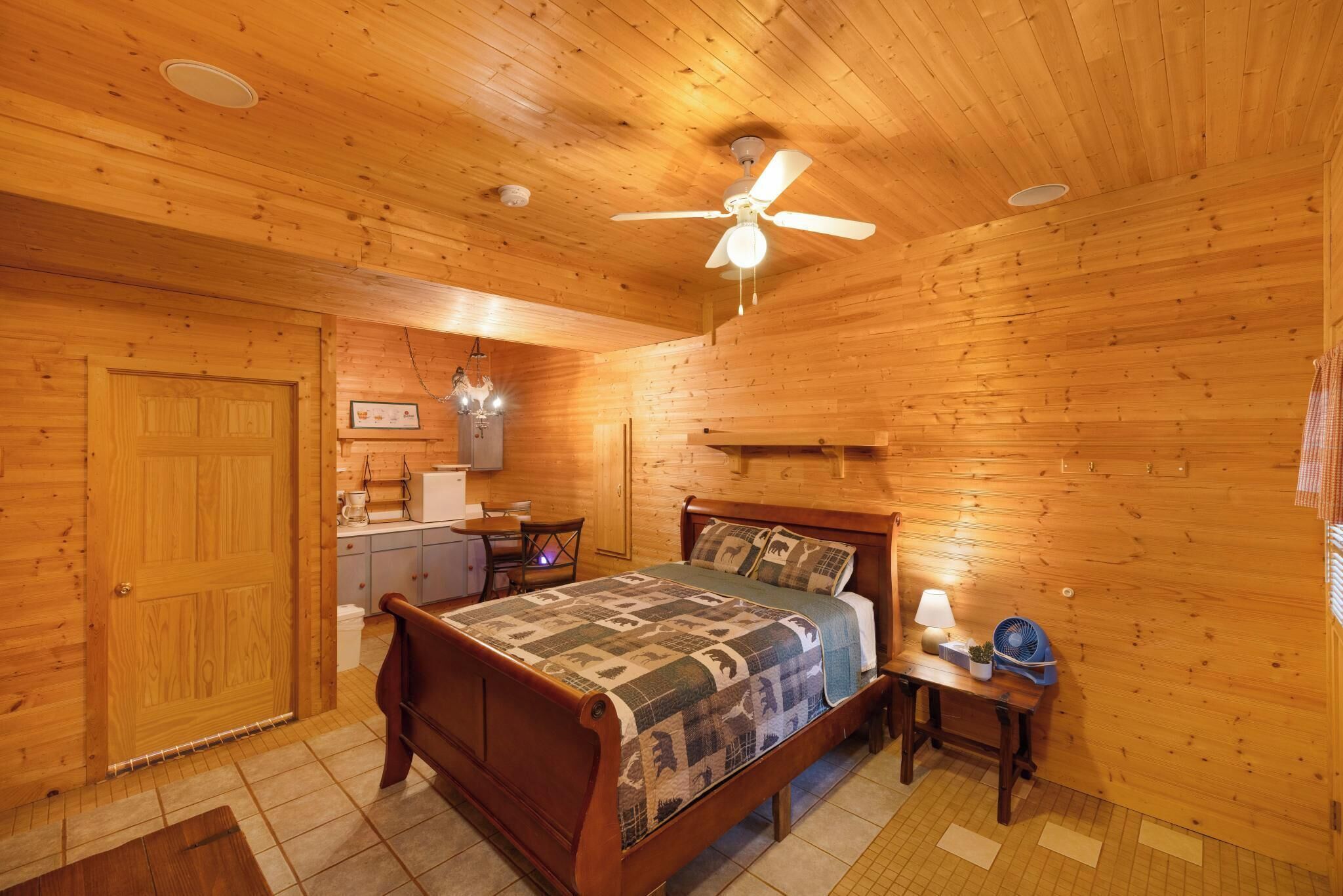 Un intérieur en bois comprenant un lit, une table de chevet, une lampe et un ventilateur de plafond.