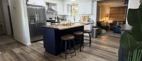 Una cocina moderna con una isla central, taburetes de bar y un área de comedor con sofá y mesa.