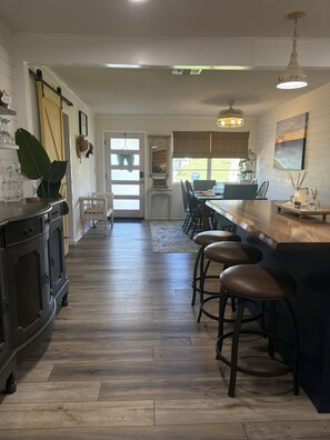 A modern kitchen with a bar area, wooden flooring, and a view to the outside. - Beachside Snowbird Retreat- 4BR/3BA,  2-Min Walk to the beach- Pet Friendly! (Port Orange)