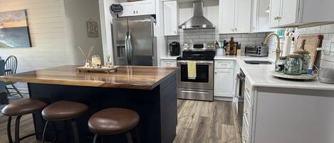 Una cocina moderna con una isla central, taburetes de bar, electrodomésticos de acero inoxidable y armarios blancos.