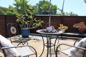 Un patio con sillas de metal, una mesa redonda y plantas en macetas.