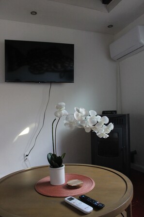 Una habitación con una mesa redonda, una planta en maceta, un control remoto y un televisor montado en la pared.