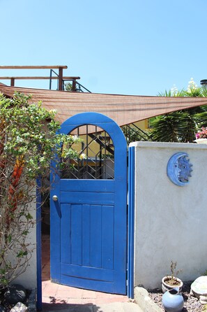 Una verja azul con reja de metal, un muro de concreto con una luna decorativa y una planta en maceta.