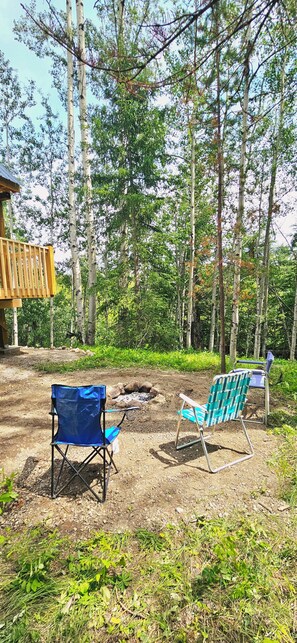 Dos sillas de camping en un área boscosa con una estructura de madera al fondo.