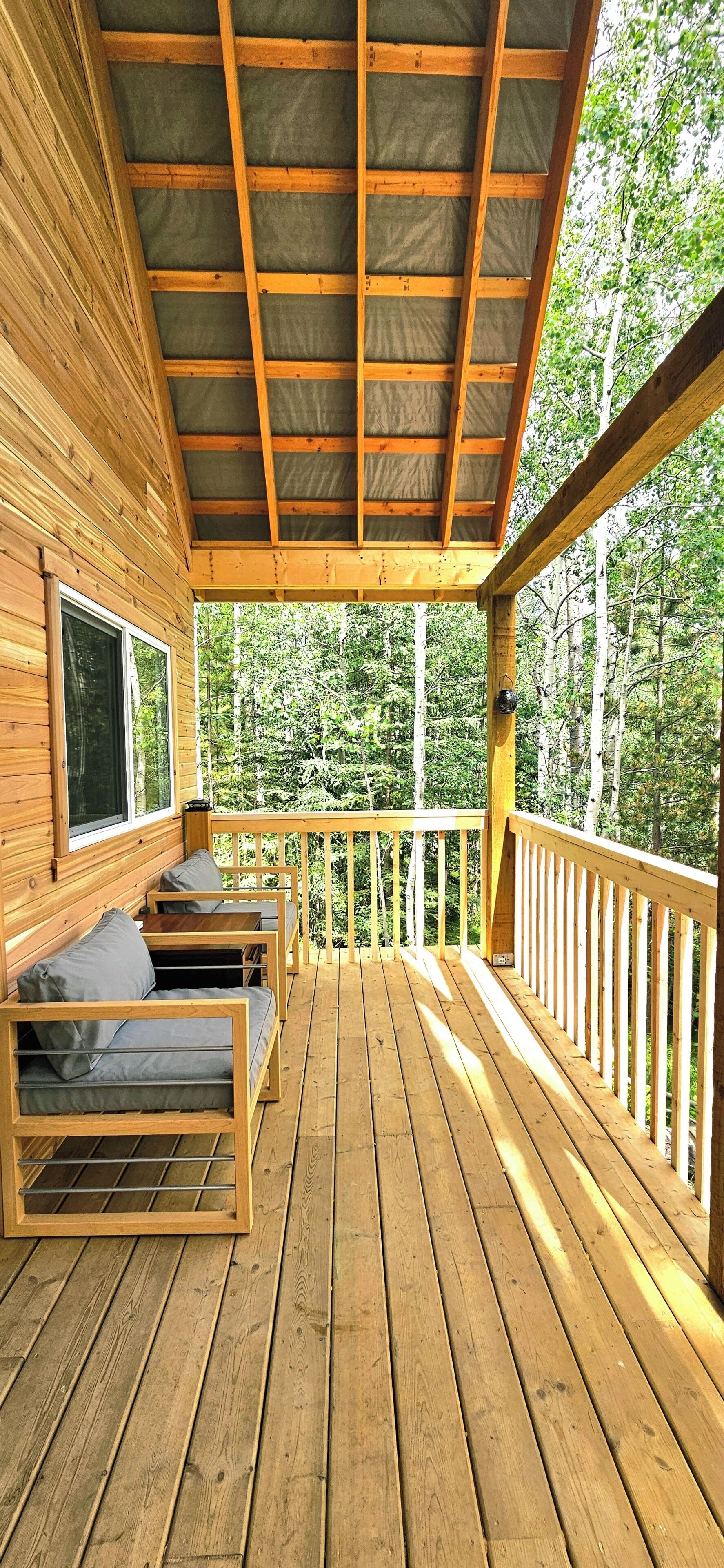 Eine Holzterrasse mit überdachter Sitzgelegenheit und Blick auf einen Wald.