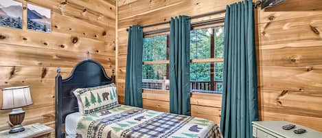 Quarto de cabana de madeira com cama, mesa de cabeceira, mesa e janela com cortinas.