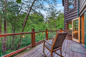 A wooden deck with a chair and railing, overlooking a forested area. - Free Dollywood Tix/Theater/Pool Table/Spacious (Sevierville)