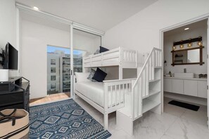 Ein modernes Schlafzimmer mit Etagenbett, Fernseher, einem gemusterten Teppich und Blick auf die Stadt durch große Fenster.