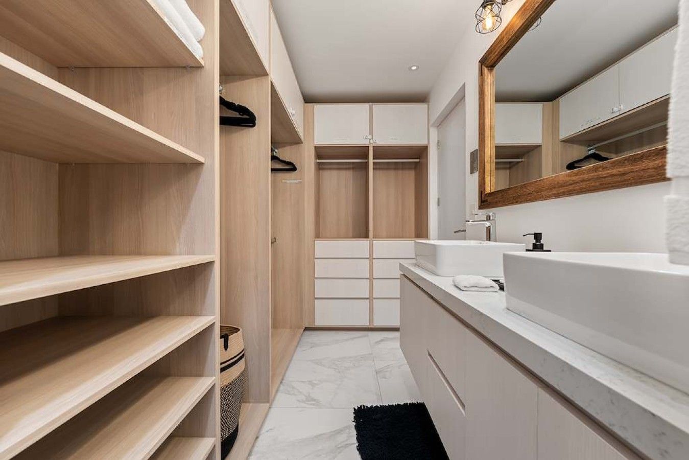 A modern bathroom with a built-in vanity, a large mirror, and a walk-in closet with wooden shelves.