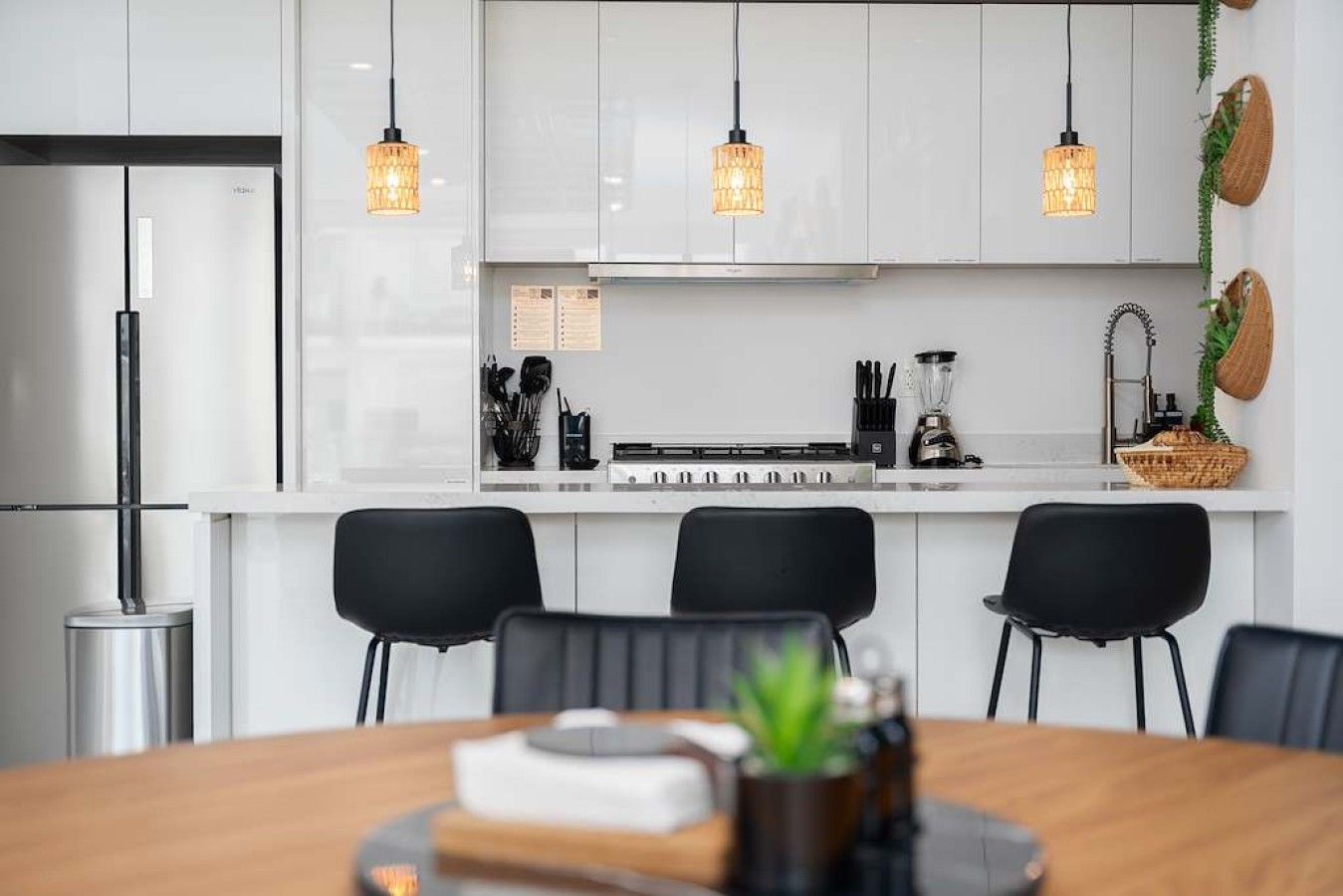 A modern kitchen with white cabinets, black chairs, and pendant lighting.