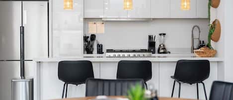 A modern kitchen with white cabinets, black chairs, and pendant lighting.