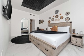 Een moderne slaapkamer met een groot bed, een flatscreen televisie aan de muur en een plafond met een geometrisch patroon.