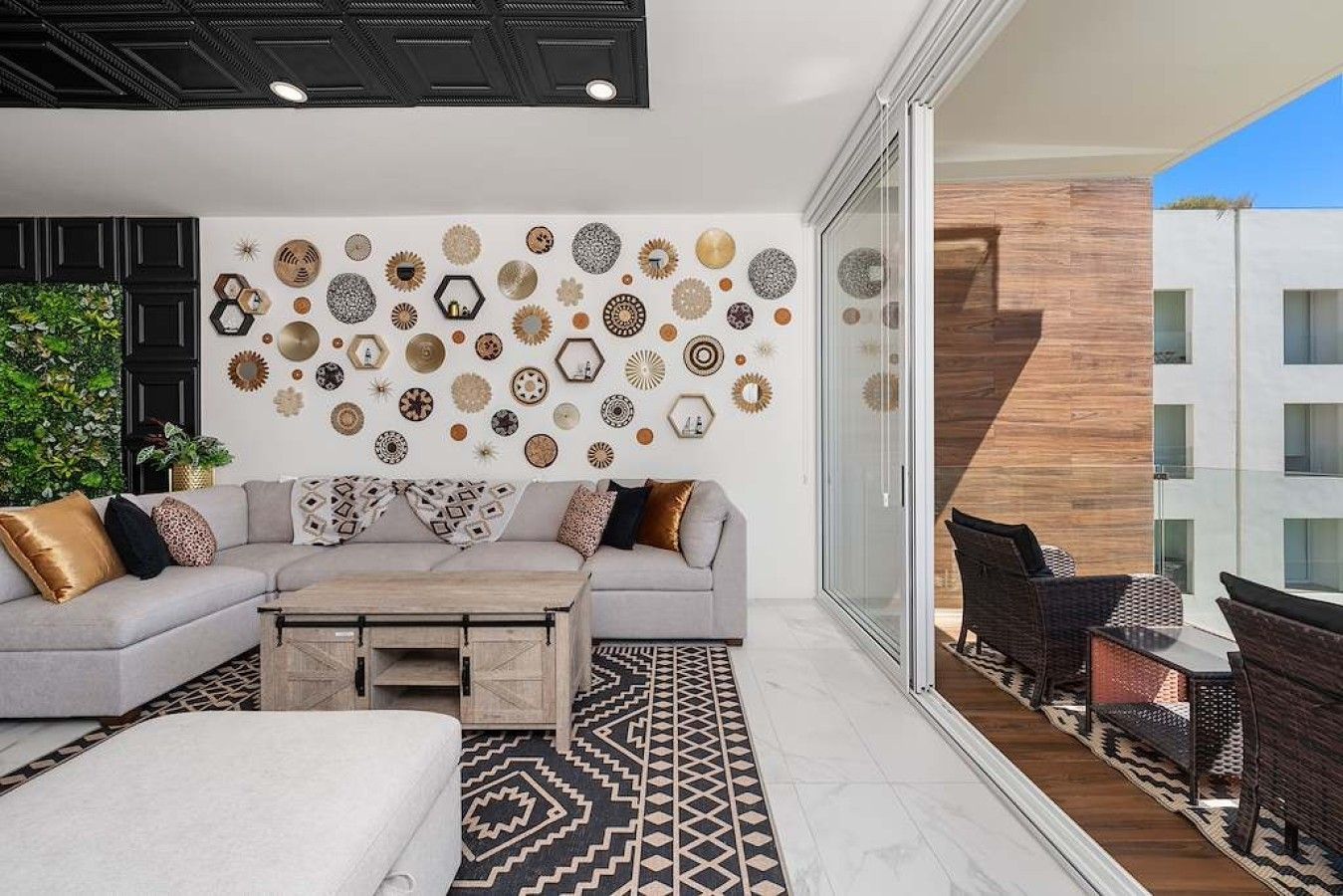 A modern living room with a grey sofa, patterned cushions, a coffee table, and a wall decorated with various wall art.