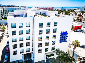 Ein mehrstöckiges Hotel mit modernem Design, das sich durch ein markantes blaues geometrisches Muster an der Fassade, mehrere Balkone und einen Blick auf die umliegende Stadt auszeichnet.